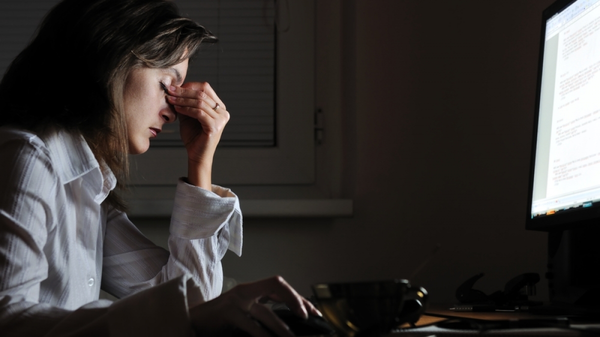 Young tired business woman with headache sitting at computer in workplace - night overtime work